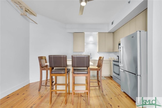 kitchen featuring light wood finished floors, a ceiling fan, cream cabinets, stainless steel appliances, and light countertops