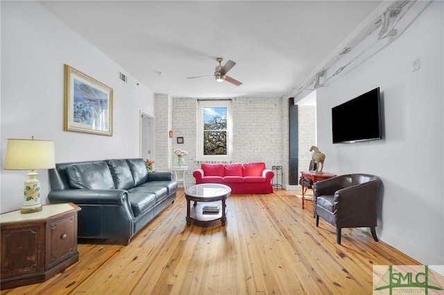 living room with visible vents, light wood-type flooring, brick wall, and ceiling fan