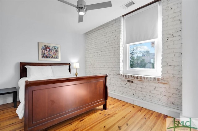 bedroom featuring wood finished floors, visible vents, brick wall, and baseboards