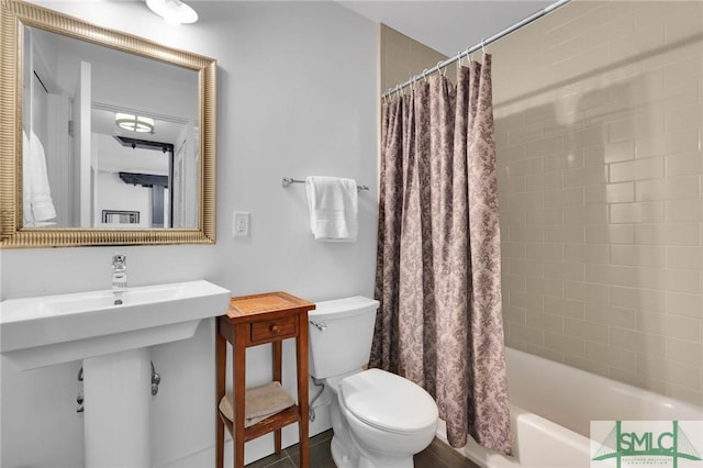 bathroom featuring a sink, shower / bath combo with shower curtain, and toilet