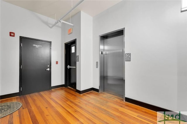 foyer with light wood-style flooring, elevator, and baseboards