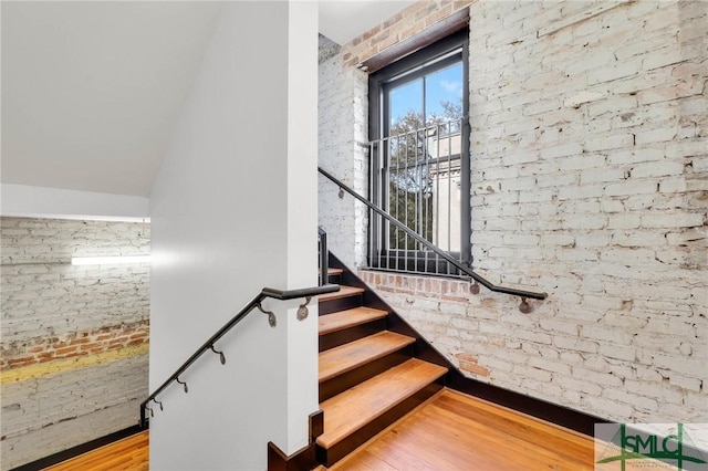 stairs featuring wood finished floors and brick wall