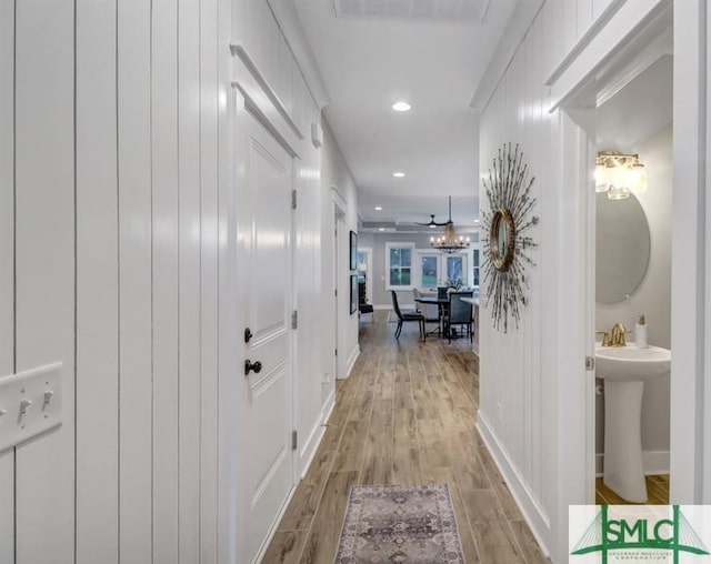 corridor with a sink, recessed lighting, light wood finished floors, baseboards, and a chandelier