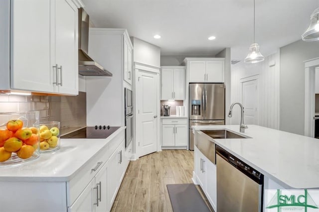 kitchen featuring a sink, white cabinetry, appliances with stainless steel finishes, wall chimney exhaust hood, and light countertops