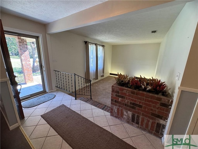 foyer with light tile patterned floors, visible vents, light colored carpet, and a textured ceiling