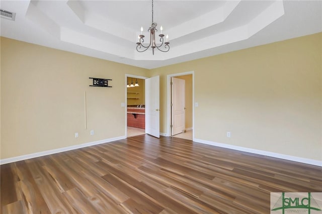 unfurnished room featuring visible vents, baseboards, a tray ceiling, an inviting chandelier, and wood finished floors