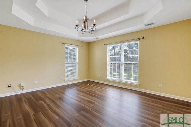 spare room featuring a tray ceiling, a notable chandelier, a healthy amount of sunlight, and visible vents