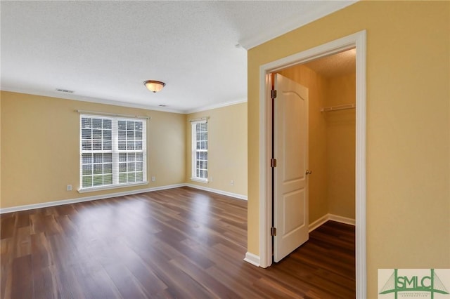 empty room featuring visible vents, ornamental molding, baseboards, and dark wood-style flooring