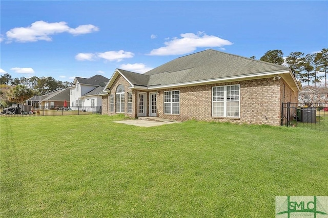 rear view of house featuring brick siding, a lawn, roof with shingles, and fence