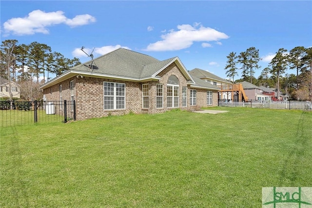 rear view of property featuring a lawn, brick siding, and fence