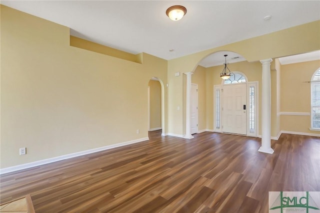 entrance foyer with decorative columns, arched walkways, baseboards, and dark wood finished floors