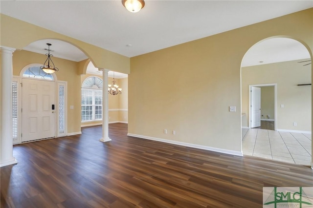 foyer with wood finished floors, arched walkways, an inviting chandelier, baseboards, and ornate columns