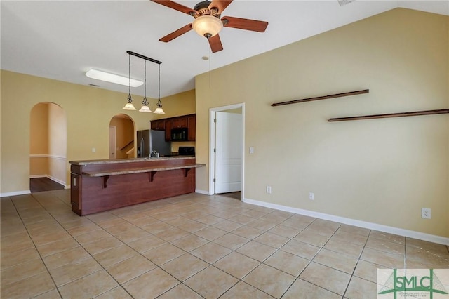 kitchen with a breakfast bar, arched walkways, black microwave, stainless steel fridge with ice dispenser, and ceiling fan