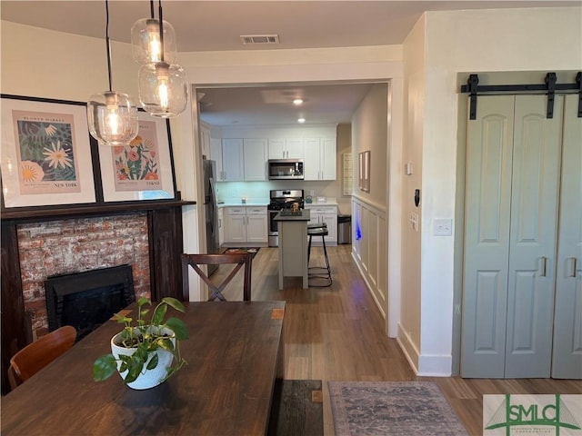 dining area with wood finished floors, visible vents, baseboards, a fireplace, and a barn door