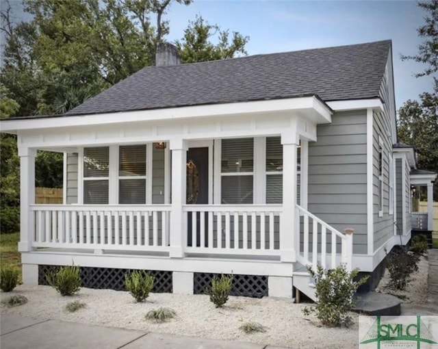 view of front of property with roof with shingles, a porch, and a chimney