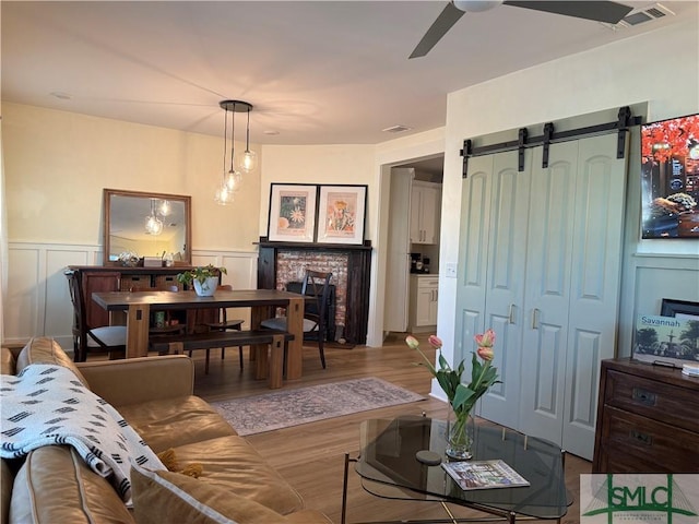 living area with visible vents, a wainscoted wall, a ceiling fan, wood finished floors, and a barn door