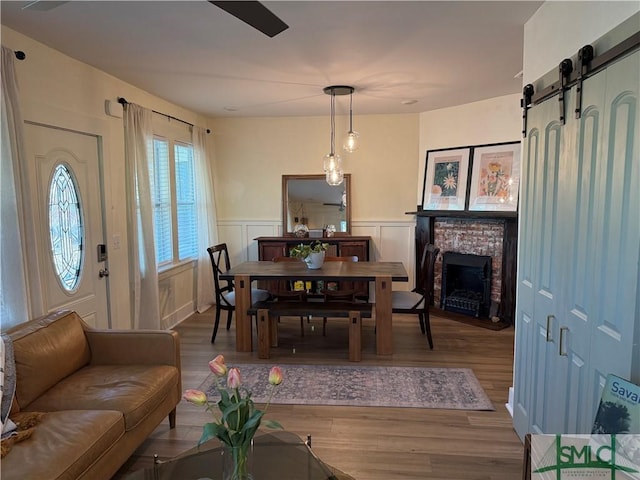 dining area with a barn door, a fireplace, wood finished floors, and wainscoting