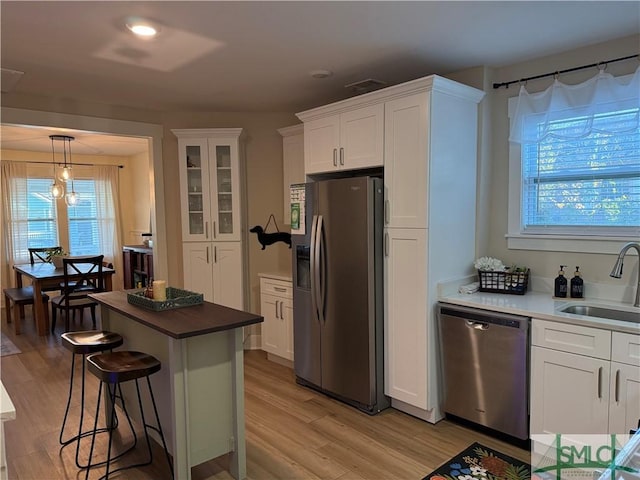 kitchen with appliances with stainless steel finishes, white cabinetry, light wood-style floors, and a sink