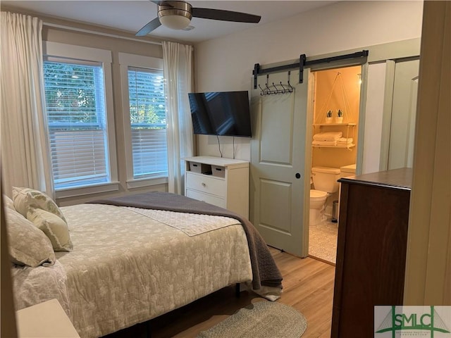 bedroom with a barn door, a ceiling fan, light wood-style flooring, and ensuite bathroom