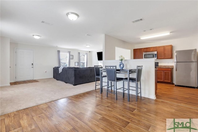 kitchen featuring visible vents, open floor plan, stainless steel appliances, a breakfast bar area, and brown cabinetry