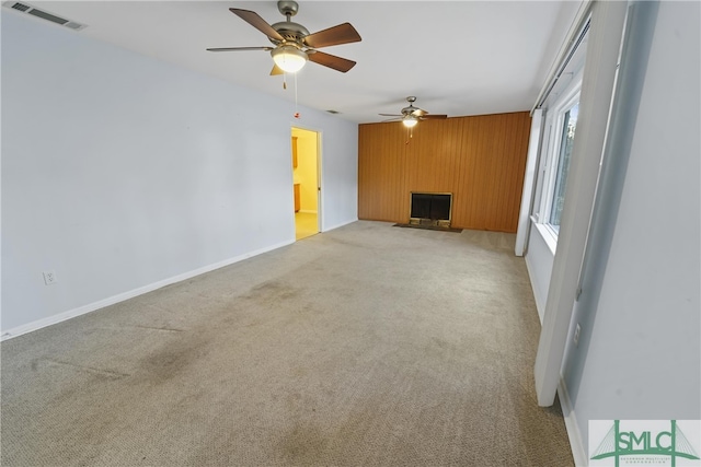 unfurnished living room featuring wooden walls, visible vents, a fireplace with flush hearth, ceiling fan, and light colored carpet