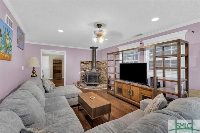 living area featuring a ceiling fan, a textured ceiling, wood finished floors, crown molding, and a wood stove