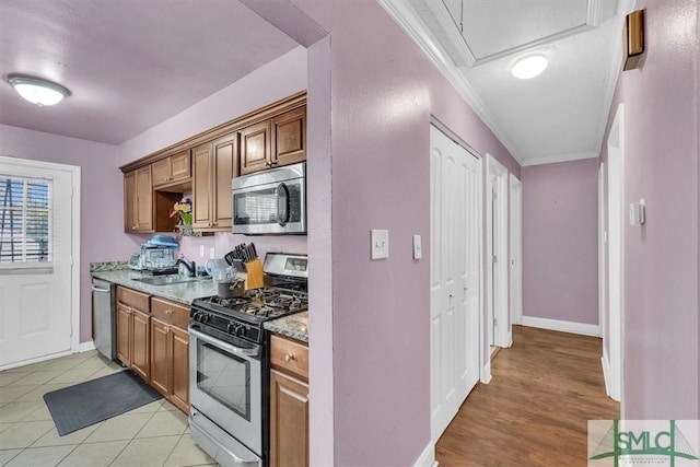 kitchen with light stone counters, a sink, stainless steel appliances, crown molding, and baseboards