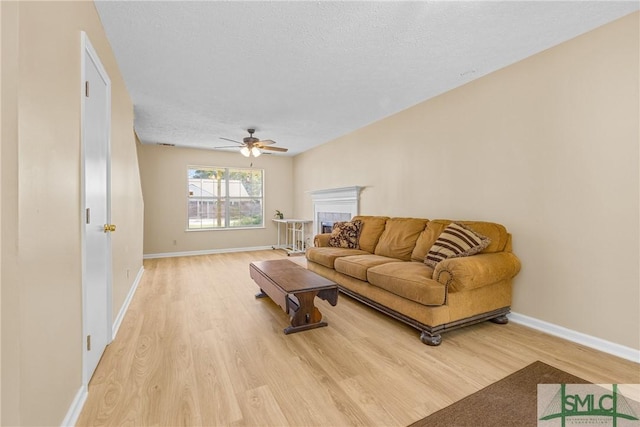 living room featuring baseboards, a textured ceiling, light wood-style flooring, and a ceiling fan