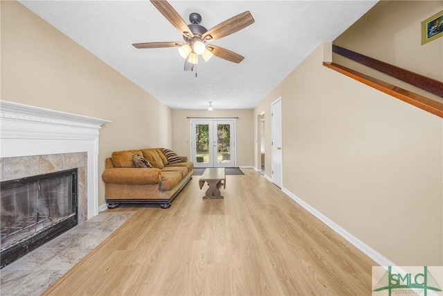 living room featuring light wood-type flooring, baseboards, ceiling fan, and a tiled fireplace