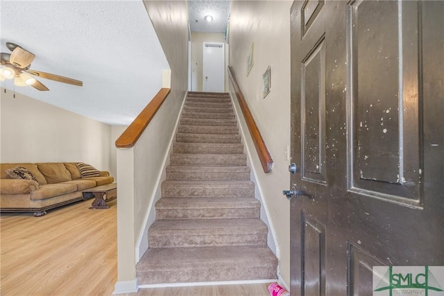 stairs featuring baseboards, a textured ceiling, a ceiling fan, and wood finished floors