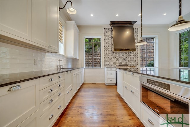 kitchen with a healthy amount of sunlight, dark countertops, custom exhaust hood, a sink, and stainless steel oven