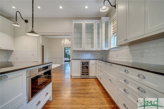 kitchen with light wood-style flooring, wine cooler, white cabinets, wainscoting, and dark countertops