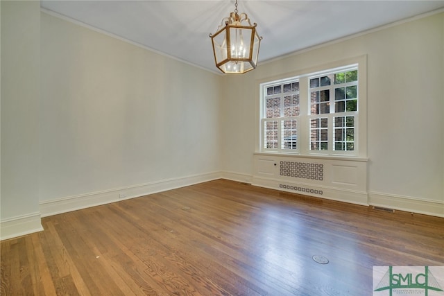 spare room with visible vents, a notable chandelier, wood finished floors, crown molding, and baseboards