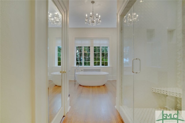 bathroom with a soaking tub, a notable chandelier, wood finished floors, and a stall shower