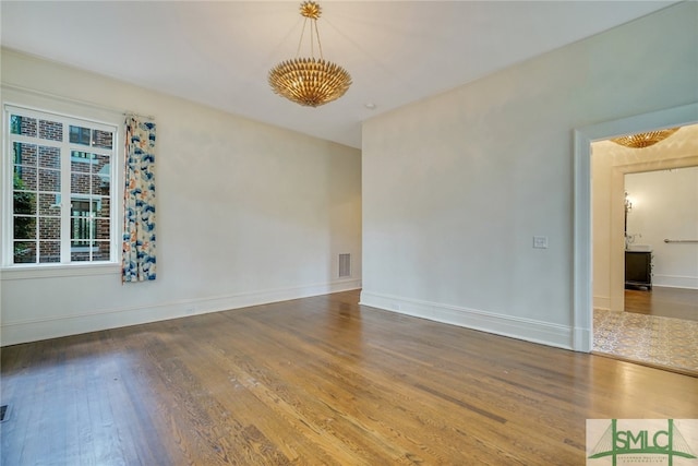 unfurnished room featuring an inviting chandelier, wood finished floors, visible vents, and baseboards