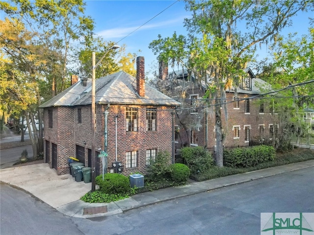 view of property exterior featuring a garage, brick siding, concrete driveway, and a chimney