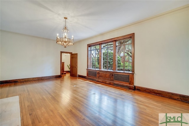 empty room featuring a chandelier, baseboards, wood finished floors, and ornamental molding