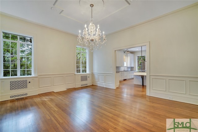 unfurnished dining area featuring visible vents, ornamental molding, light wood-style floors, an inviting chandelier, and a decorative wall