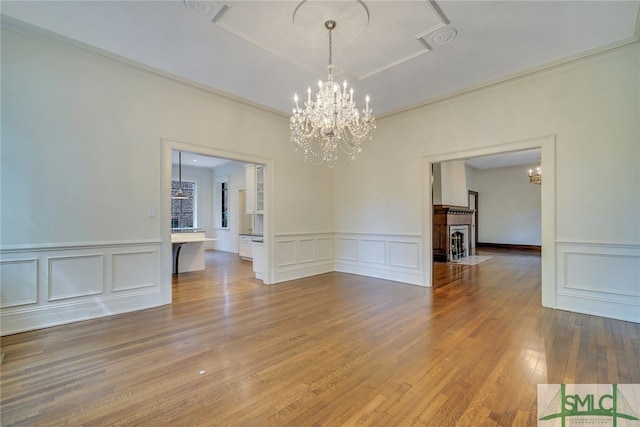 unfurnished room featuring an inviting chandelier, wood finished floors, crown molding, and a decorative wall