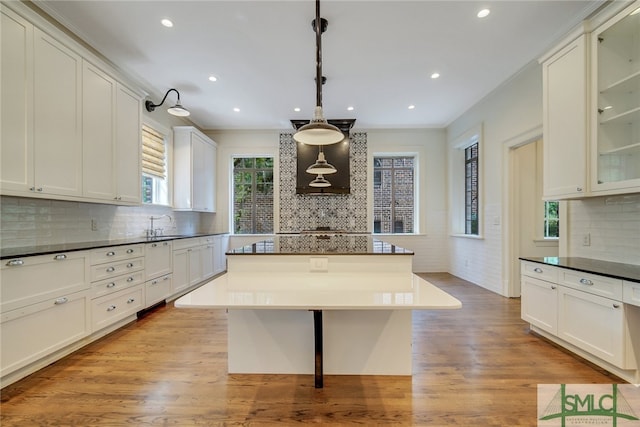 kitchen with light wood-type flooring, glass insert cabinets, and dark countertops