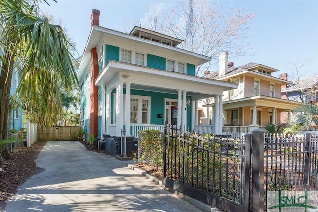 traditional style home with driveway, covered porch, a fenced front yard, and a chimney