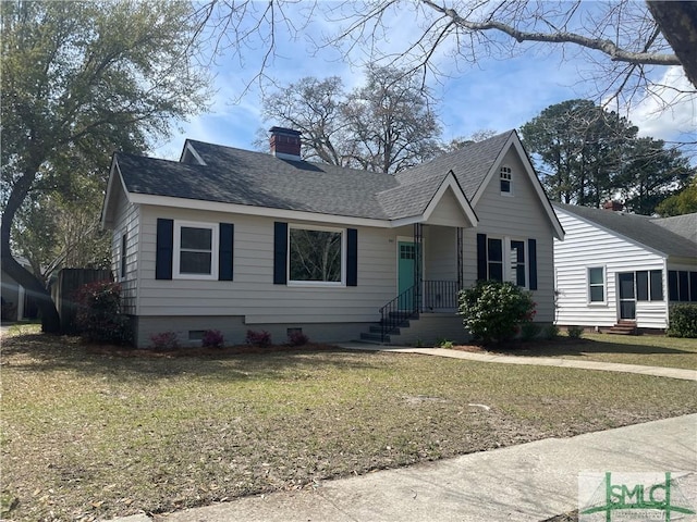 view of front facade with a front yard, roof with shingles, and a chimney