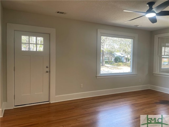 foyer entrance with visible vents, a textured ceiling, baseboards, and wood finished floors