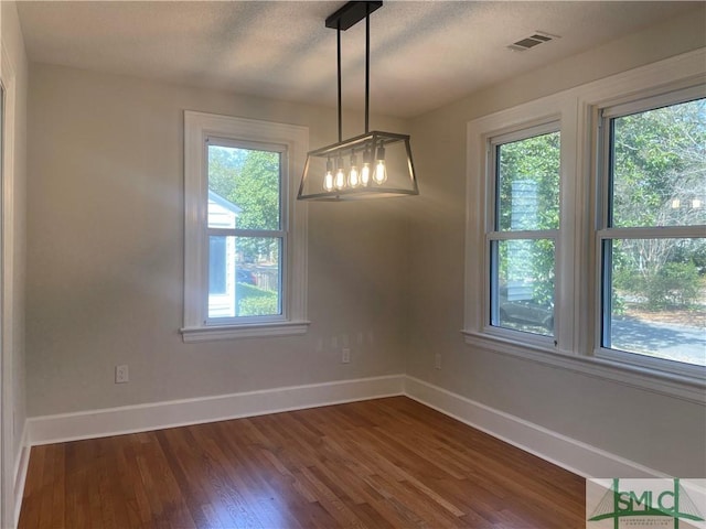 unfurnished dining area featuring dark wood-style floors, visible vents, a textured ceiling, and baseboards