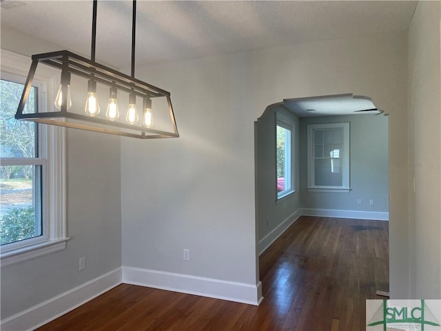 unfurnished dining area featuring dark wood finished floors, plenty of natural light, and baseboards