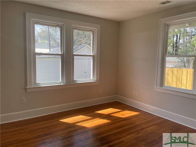 spare room featuring visible vents, baseboards, dark wood-style flooring, and a textured ceiling