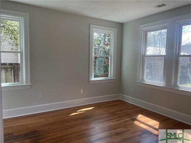 unfurnished room featuring dark wood-style floors, visible vents, and plenty of natural light