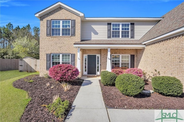 property entrance featuring brick siding, a lawn, and fence