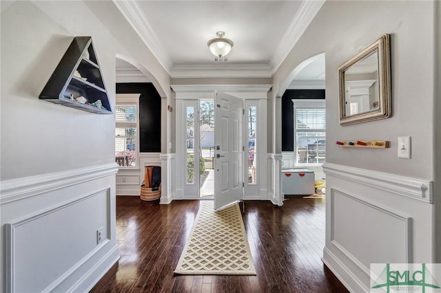 entrance foyer with a wainscoted wall, dark wood-type flooring, arched walkways, and ornamental molding