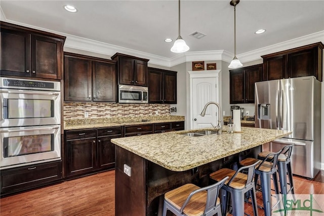 kitchen with light stone countertops, appliances with stainless steel finishes, wood finished floors, and a sink